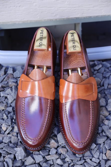 A pair of brown leather loafers with a tan bow detail and wooden shoe trees inside.