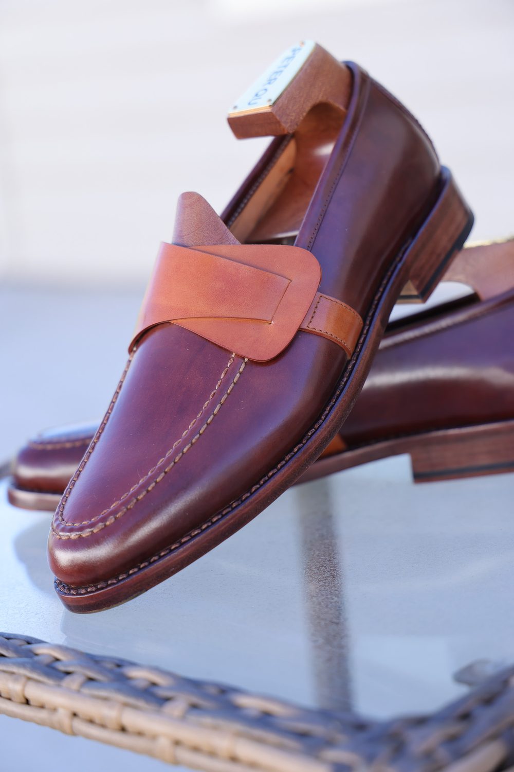 A pair of brown leather loafers with a tan strap and stitching detail.