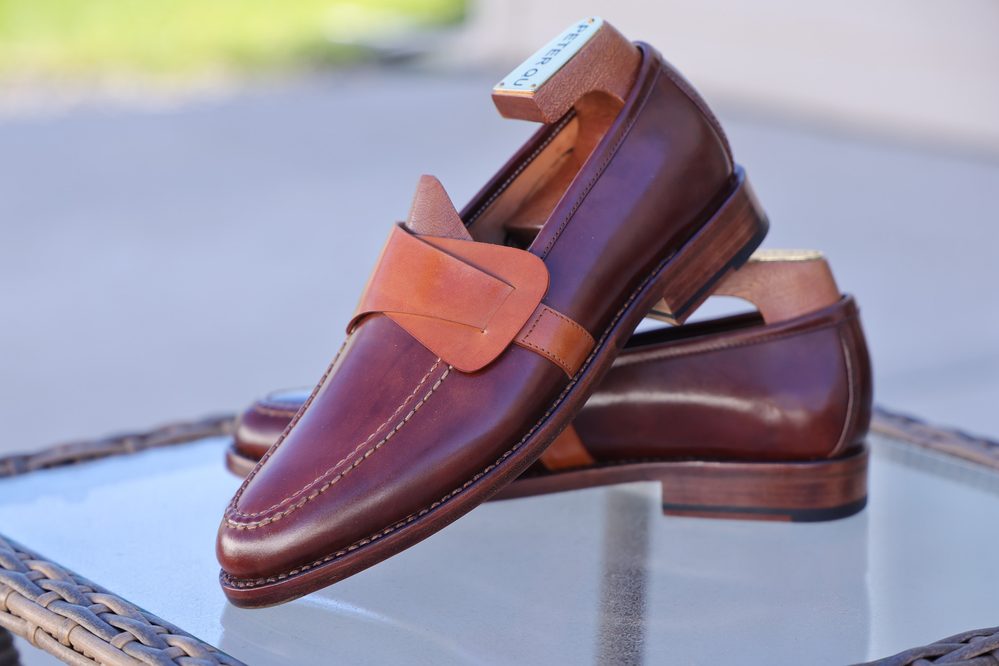 A pair of brown leather loafers with a tan strap and wooden heel.