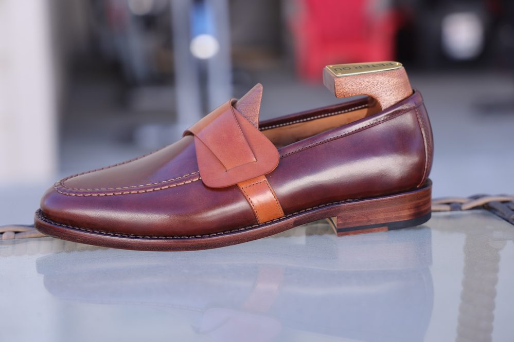 A brown leather loafer with a tan leather strap and a wooden heel.