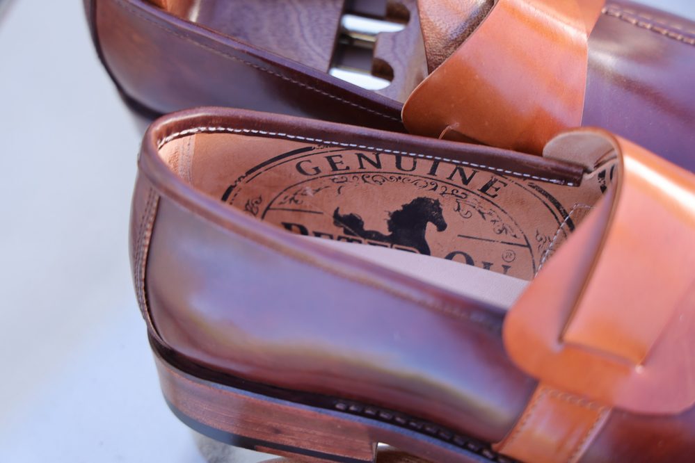 A close-up of brown leather shoes showing the interior with a logo that reads "Genuine Peter Qu."
