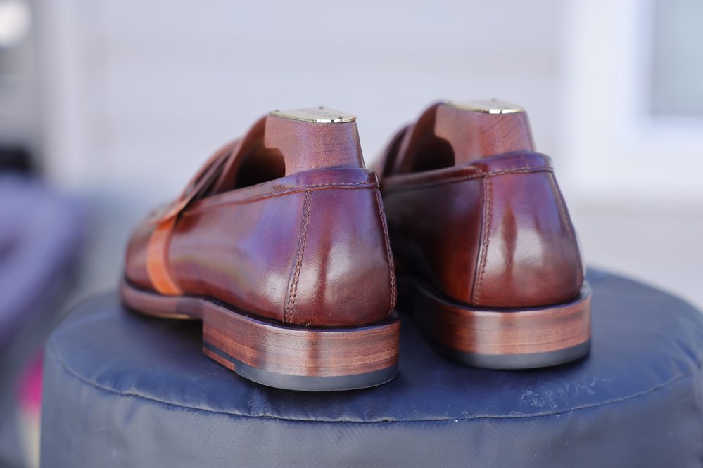 A pair of polished brown leather shoes with a wooden heel, viewed from the back.