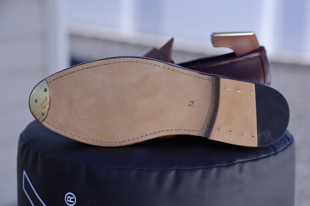 The image shows the sole of a brown leather shoe with a brass heel plate and a size marking of 7.5.