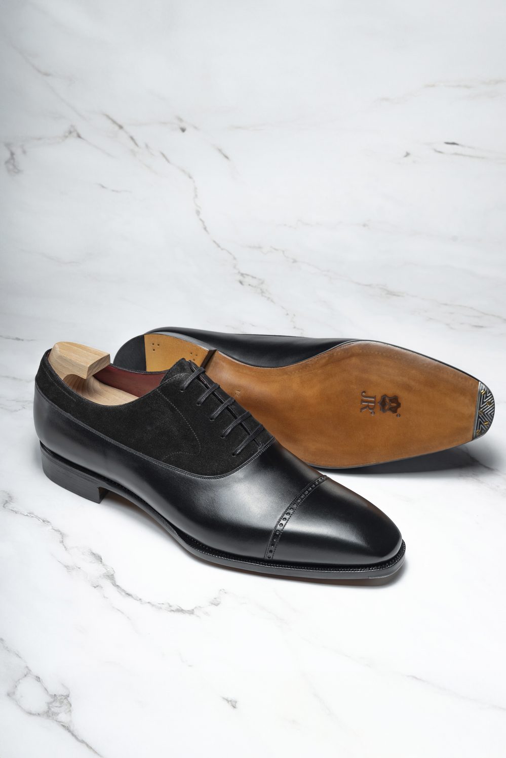 A pair of elegant black leather shoes with suede accents and wooden shoe trees.