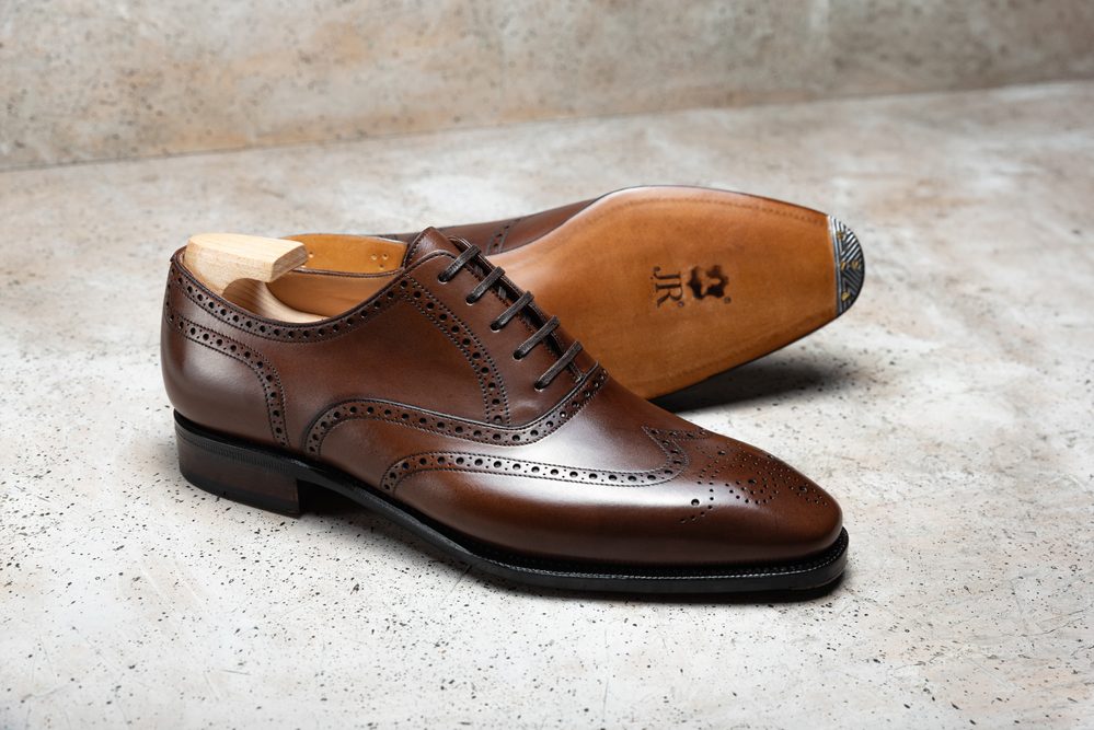 A brown leather dress shoe with brogue detailing and a wooden shoe tree inserted.