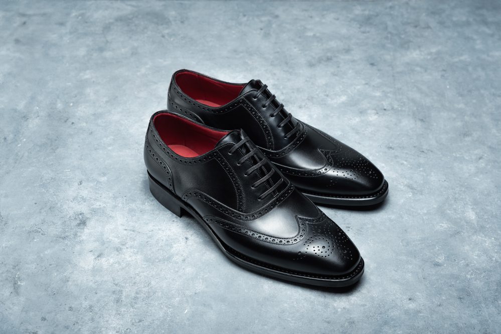 A pair of black leather dress shoes with a brogue design and red insoles.