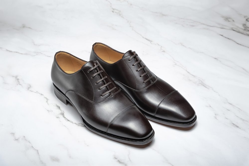 A pair of polished brown leather dress shoes with a cap toe and lace-up design.
