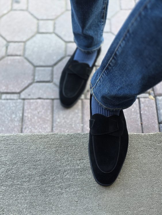 Black suede shoes with a decorative strap, paired with blue striped socks and denim jeans.