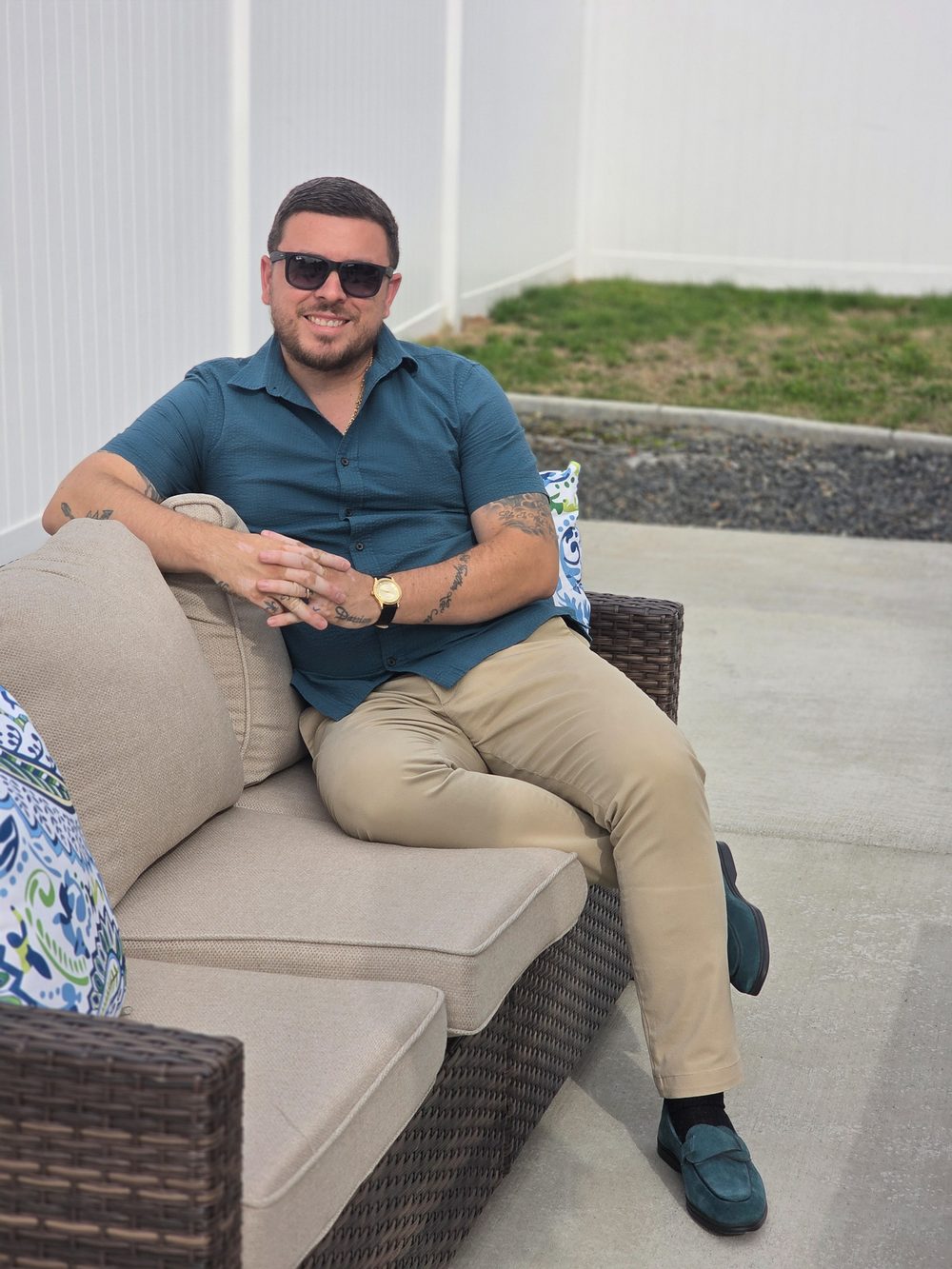 A man in sunglasses smiles while sitting on a beige couch, wearing a teal shirt and tan pants, reflecting "My New Chapter."