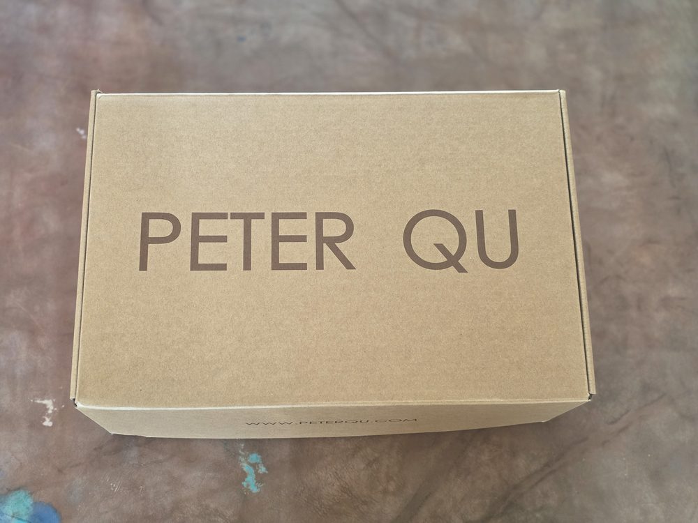 A brown cardboard box with the text "PETER QU" printed in dark brown on the top.