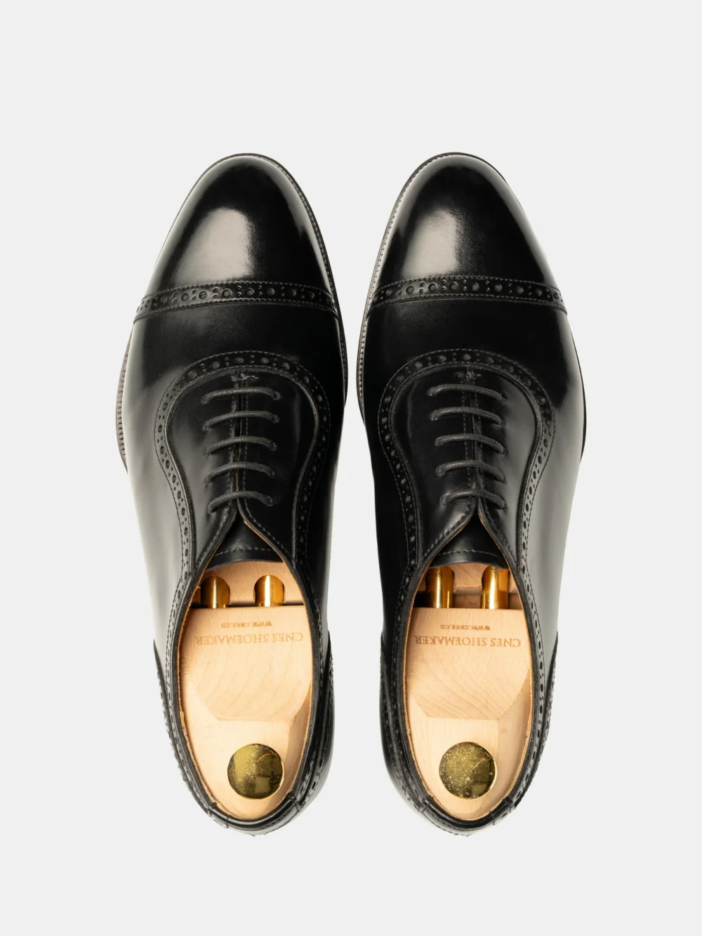 A pair of black leather dress shoes with a brogue design and wooden shoe trees inside.
