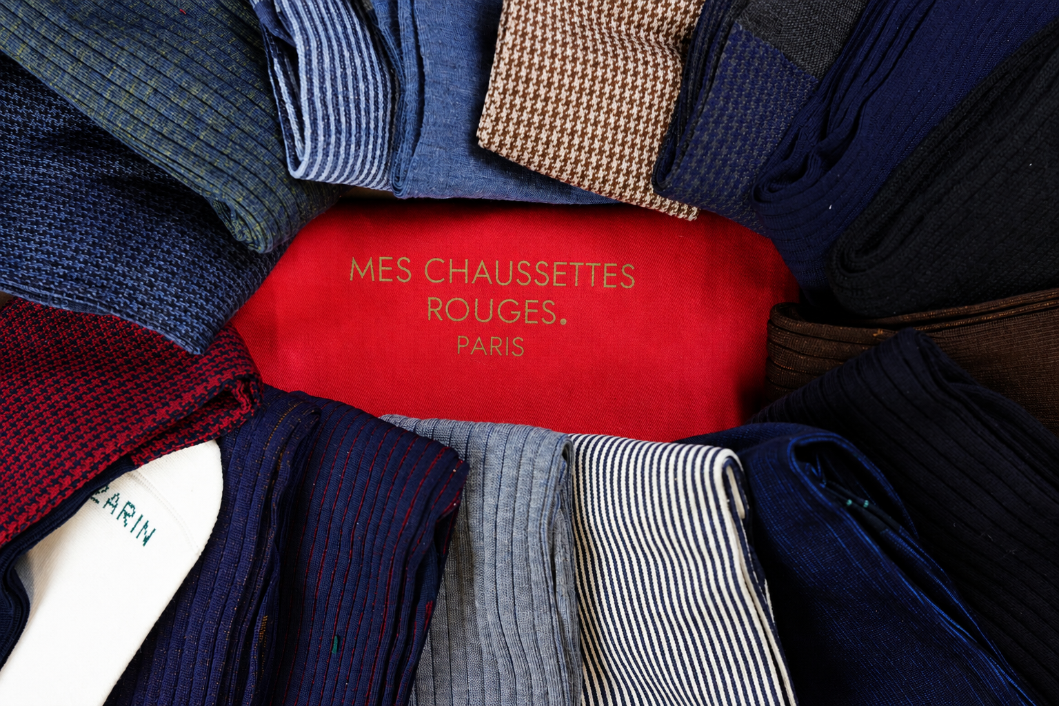 A collection of colorful socks in various patterns surrounds a red label that reads "MES CHAUSSETTES ROUGES. PARIS."