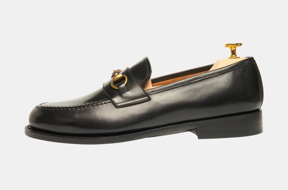 A black leather loafer with a gold buckle detail.