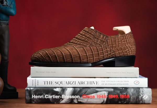 A brown crocodile-embossed leather shoe is displayed on a stack of three books.