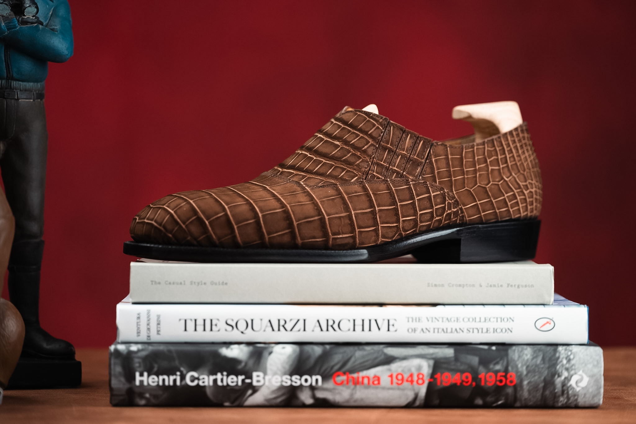 A brown crocodile-embossed leather shoe is displayed on a stack of three books.