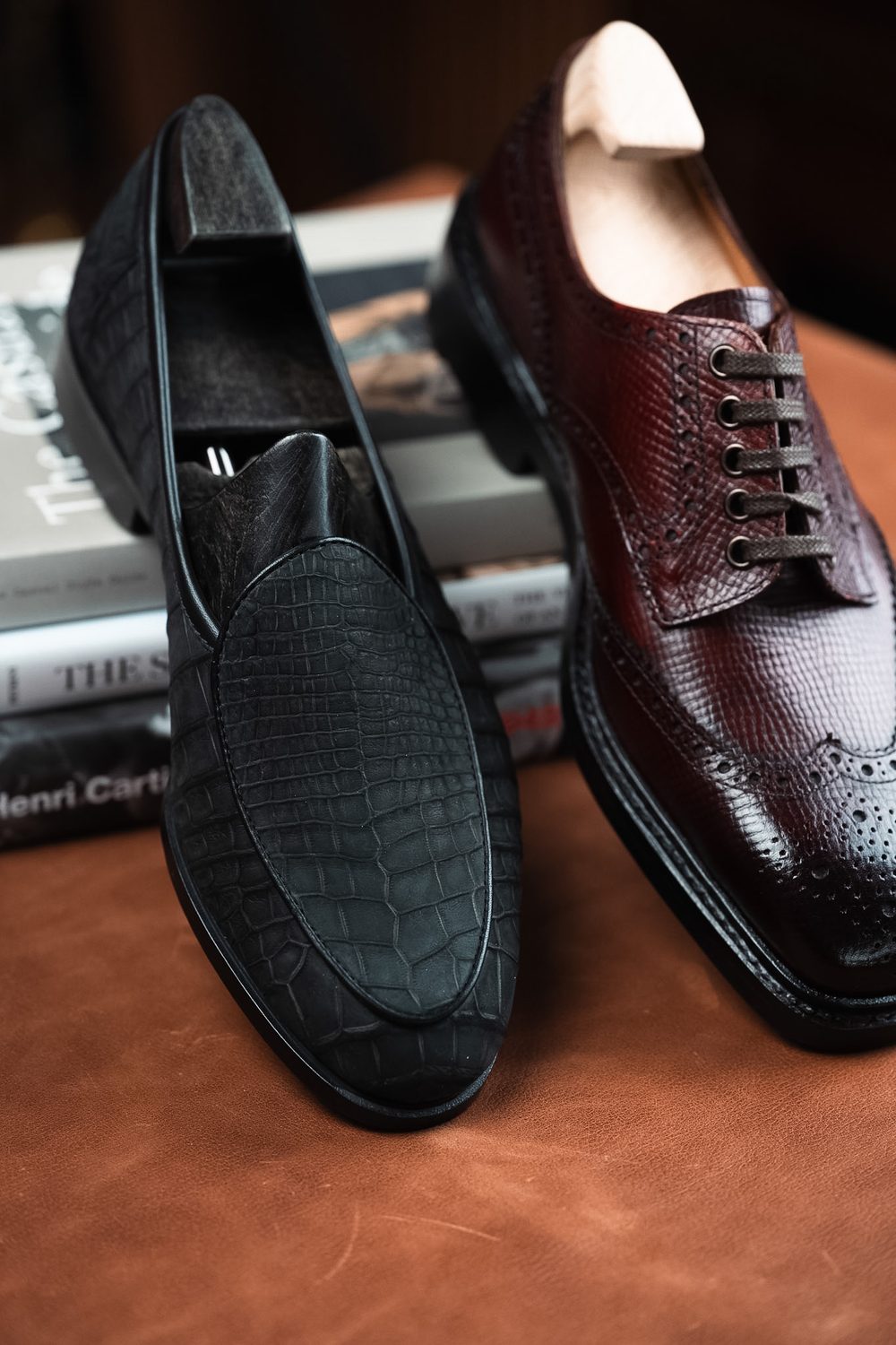 A black crocodile nubuck loafer and a burgundy crocodile leather dress shoe are displayed side by side.