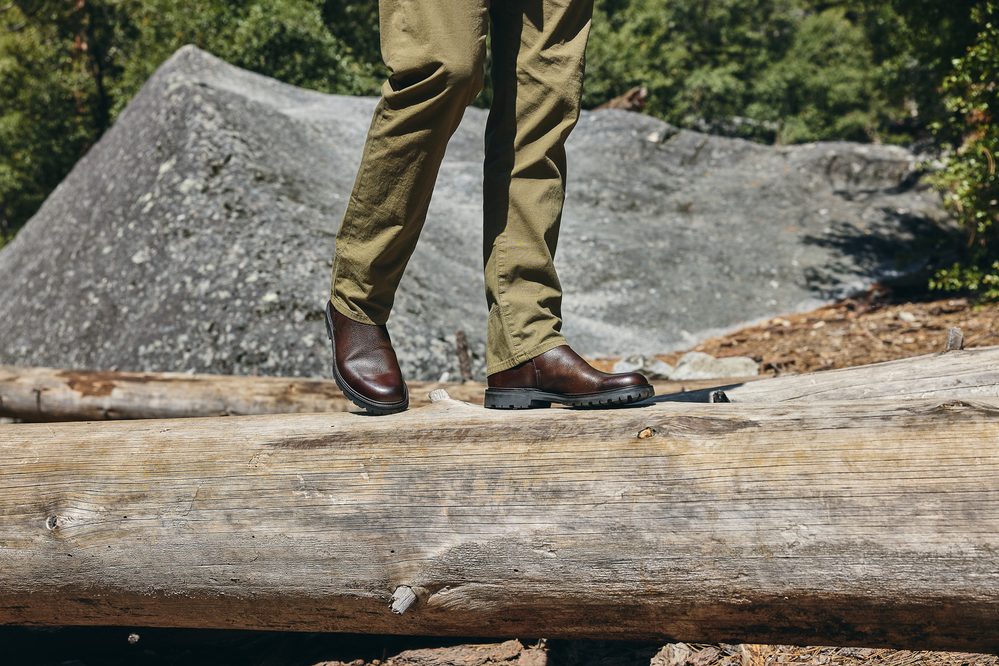 A person stands on a log wearing brown leather boots and olive green pants.