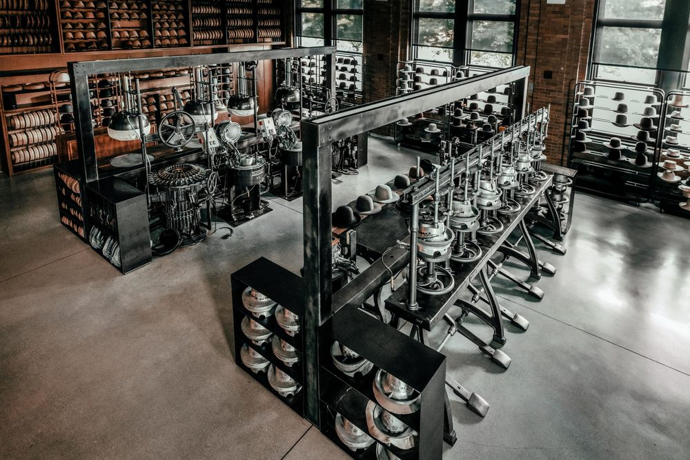 A collection of vintage hat-making machinery in black metal, with silver components, arranged in a factory setting.
