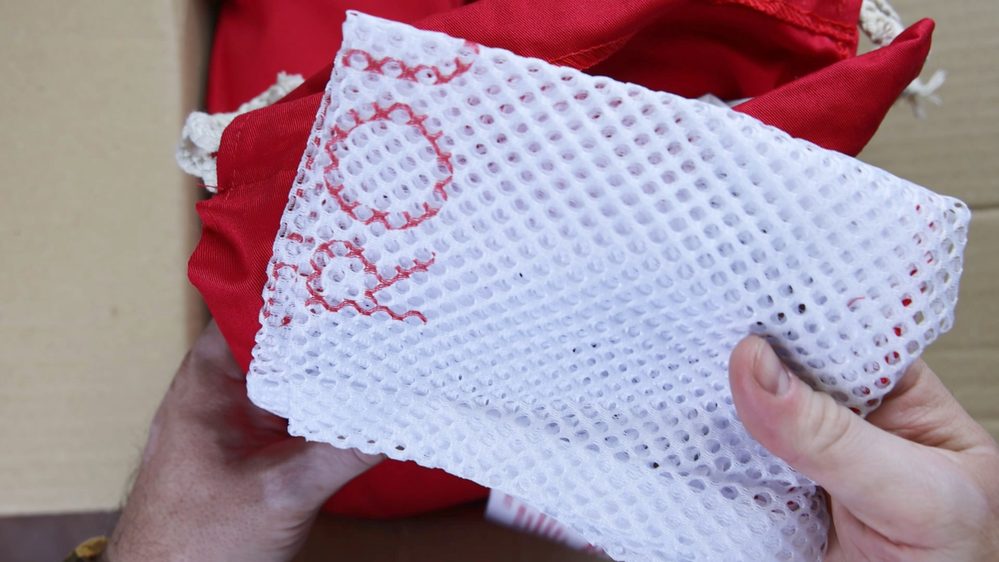 A person holds a white mesh fabric with red stitching in front of a red item.