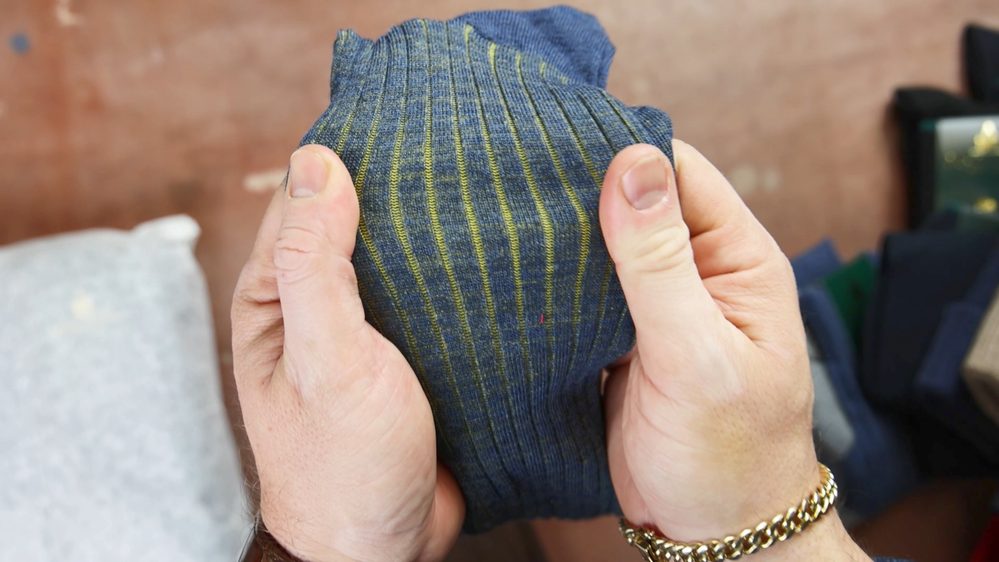 A pair of blue striped socks with yellow lines is held in two hands.