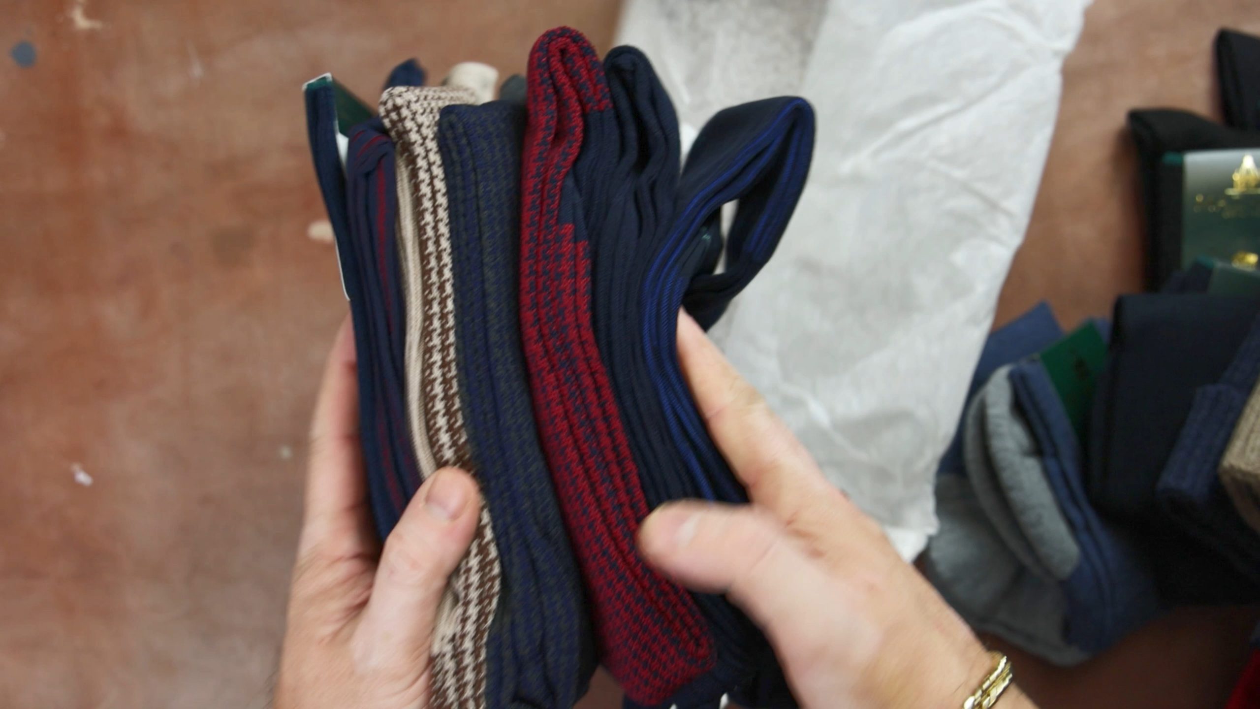 A person holds a bundle of socks in various colors, including dark blue, red, and beige.