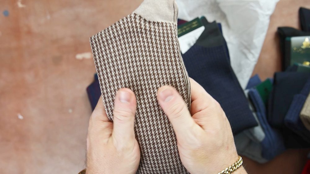 A person holds a pair of brown and beige houndstooth-patterned socks.