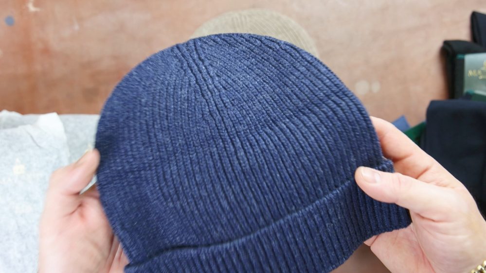 A person holds a textured navy blue knit beanie.