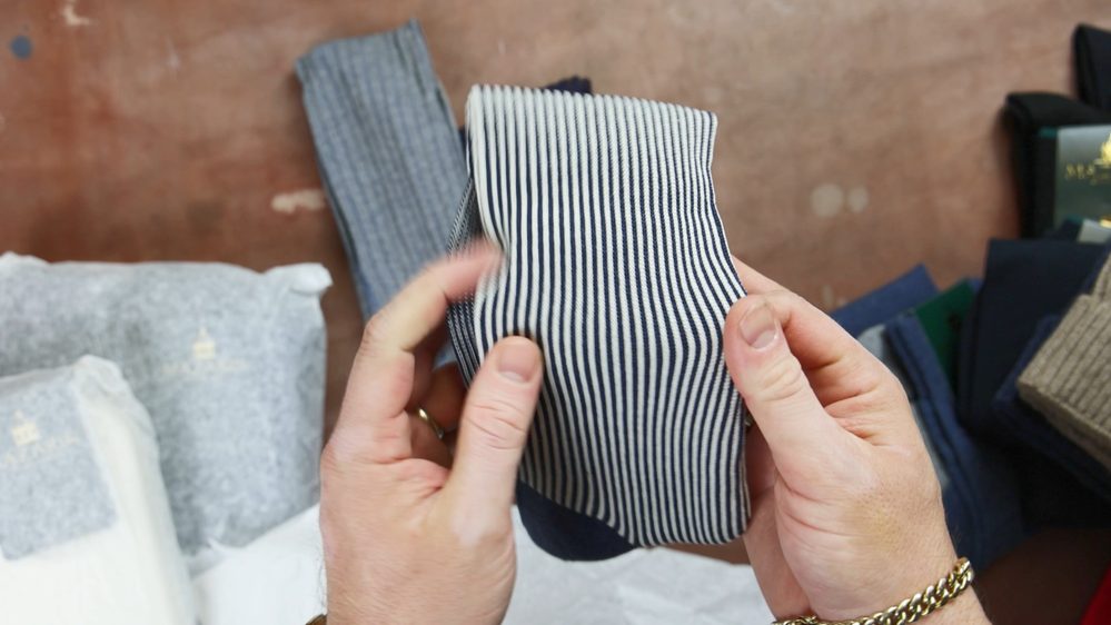 A person holds a pair of navy and white striped socks.