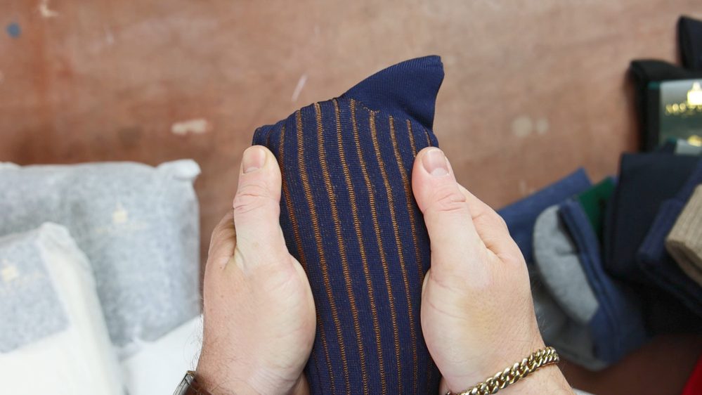 A pair of navy blue socks with brown stripes is being held in hands.