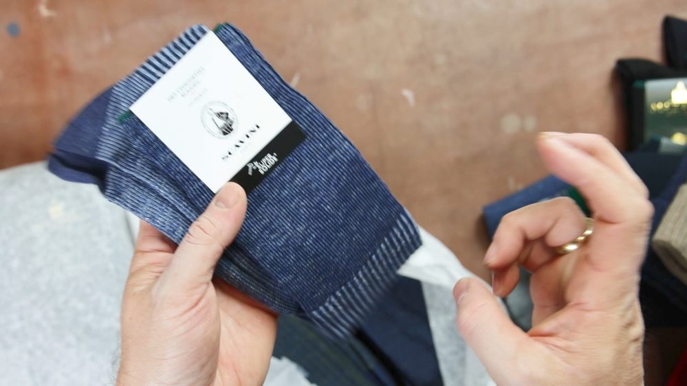 A person holds a pair of navy blue striped socks with a label from Mes Chaussettes Rouges.