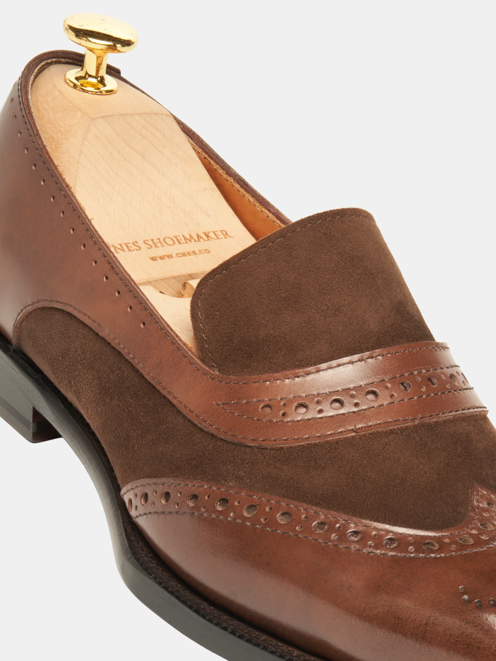 A brown leather and suede shoe with decorative brogue detailing and a gold shoe tree inside.