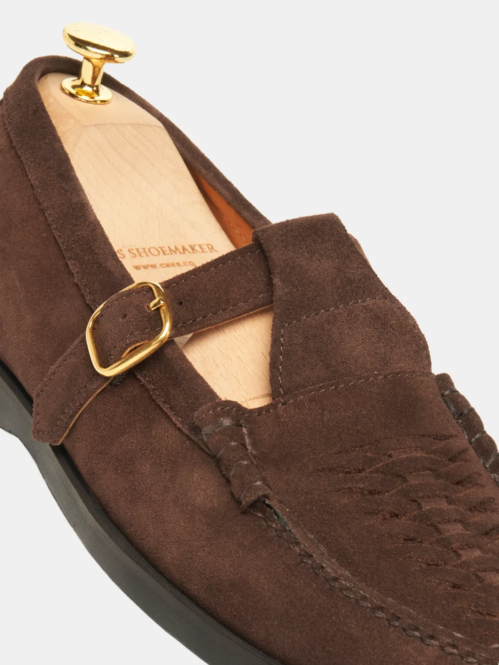 A close-up of a brown crocodile nubuck shoe featuring a gold buckle and a shoe tree inside.