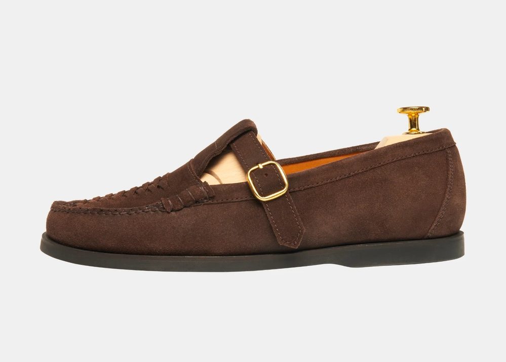 Brown suede loafers with a gold buckle and a wooden shoe tree inside.