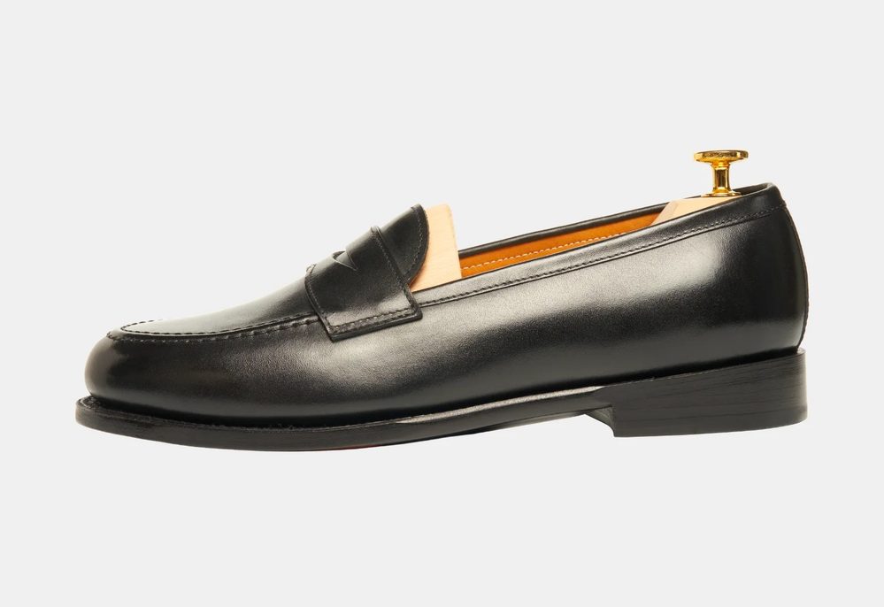 Black leather loafer with a slight heel and a wooden shoe tree inserted.