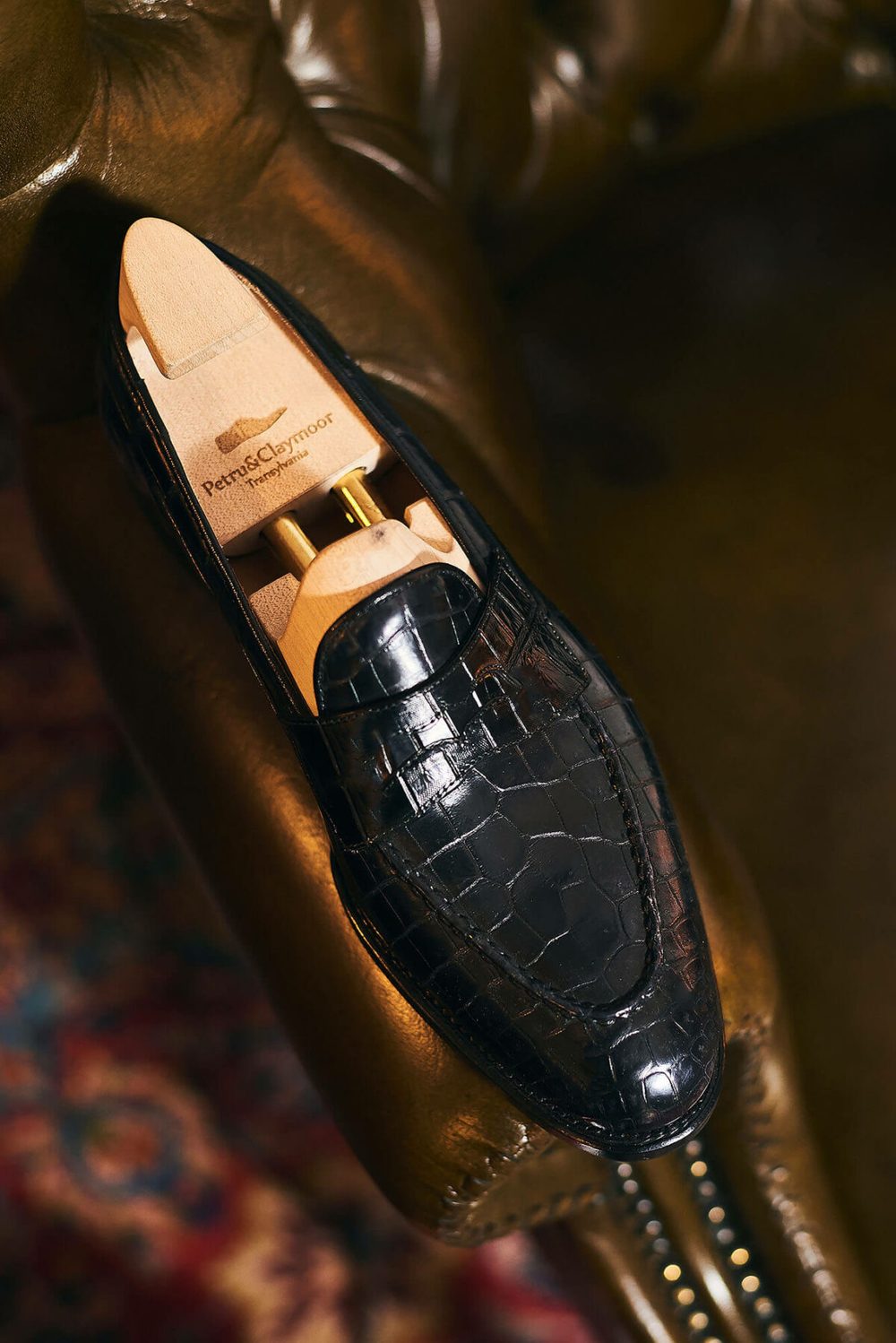A black crocodile leather shoe with a wooden shoe tree inside, featuring the brand name "Petru & Claymoor."