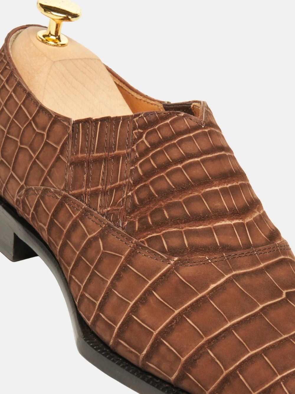 A close-up of a brown crocodile nubuck shoe with a wooden shoe tree inside.
