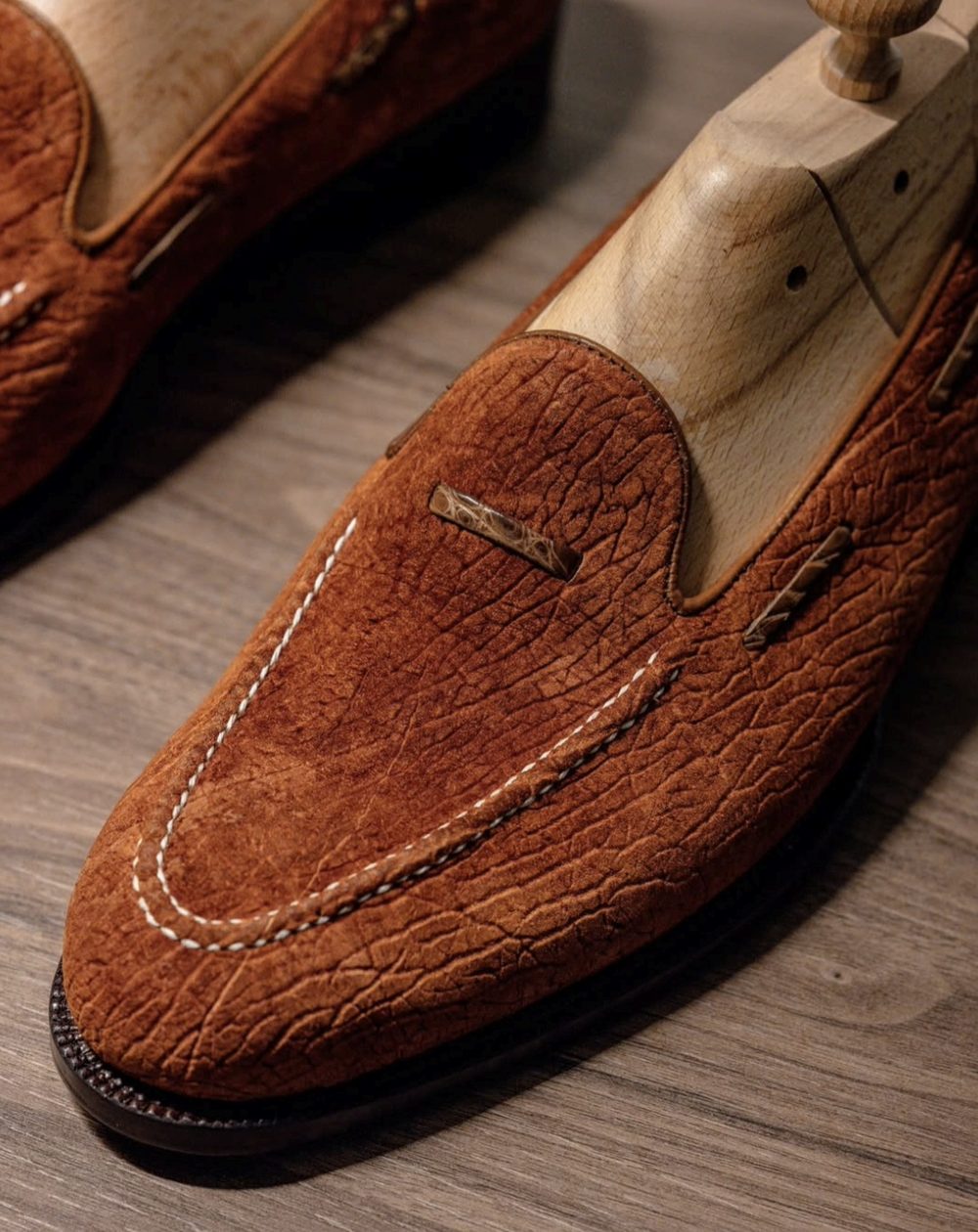 Close-up of handcrafted brown suede loafers with a textured finish and white stitching.