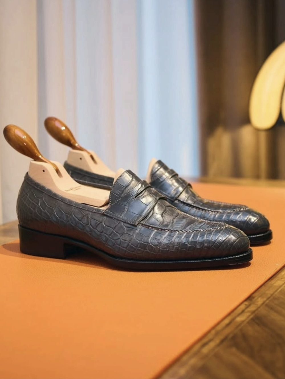 A pair of handmade gray crocodile leather shoes with wooden shoe trees.
