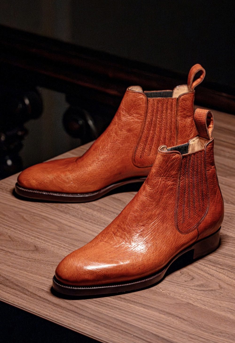 A pair of handmade leather Chelsea boots in a rich orange color, featuring elastic side panels and pull tabs.