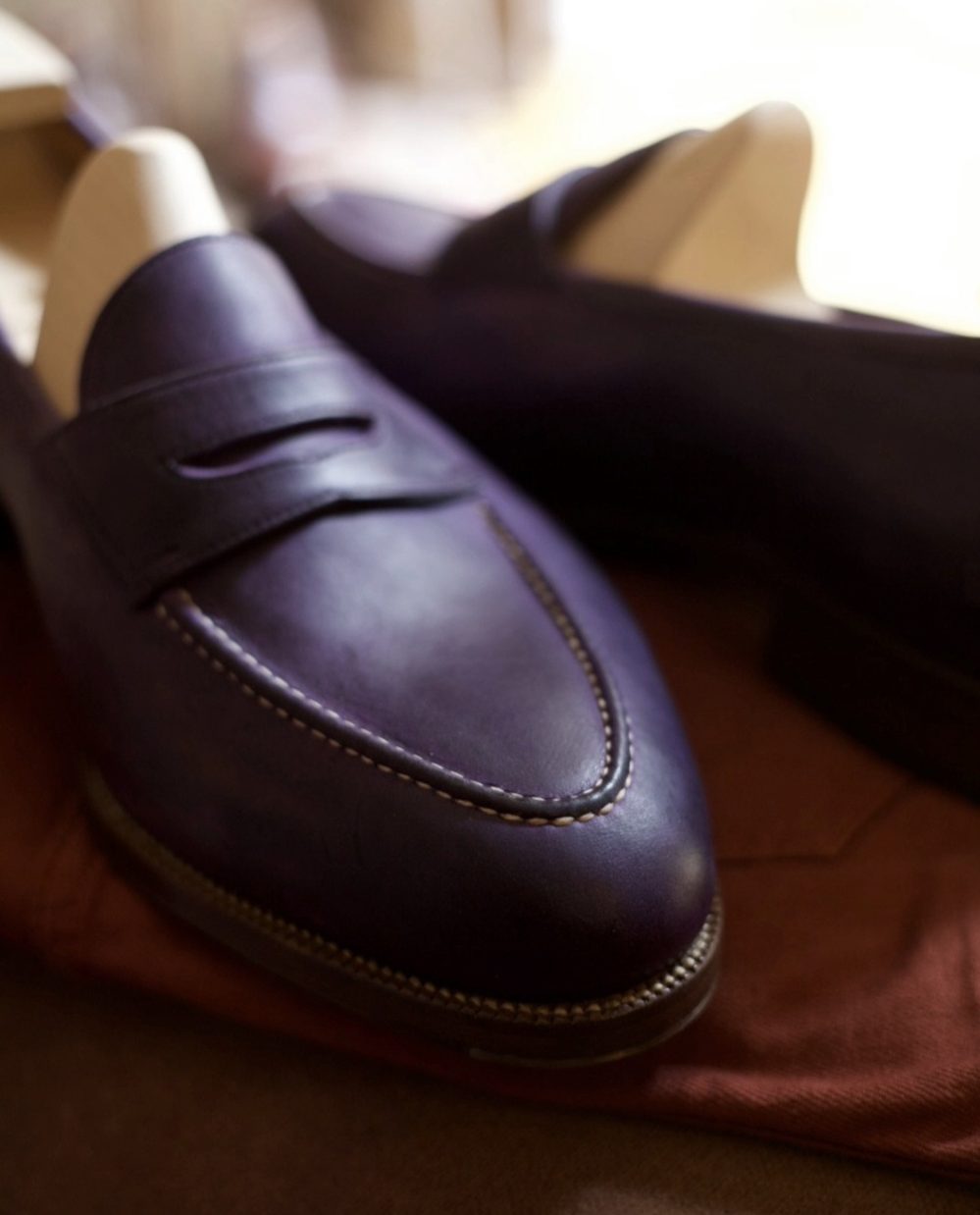 Close-up of handmade dark purple leather shoes with decorative stitching.
