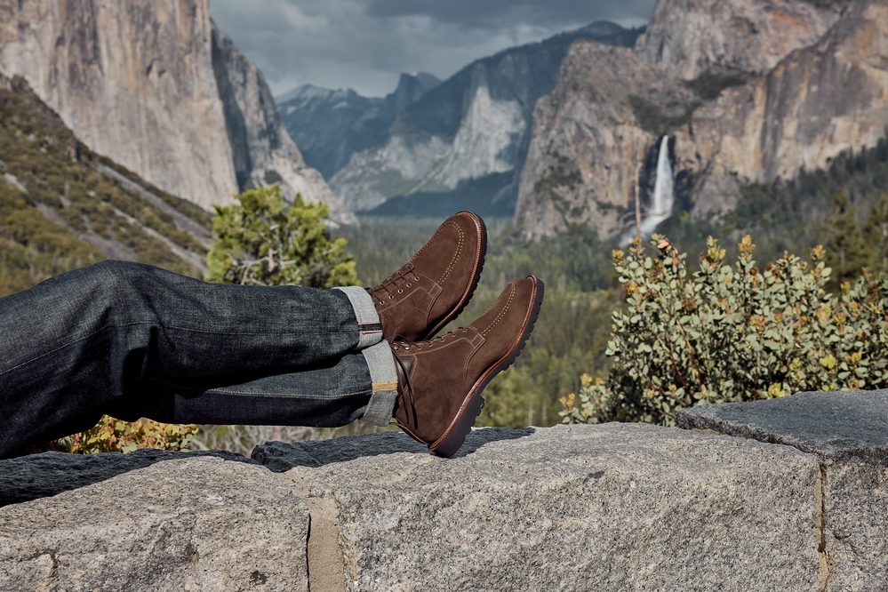 Brown suede boots resting on a stone ledge, with denim jeans rolled at the cuffs.