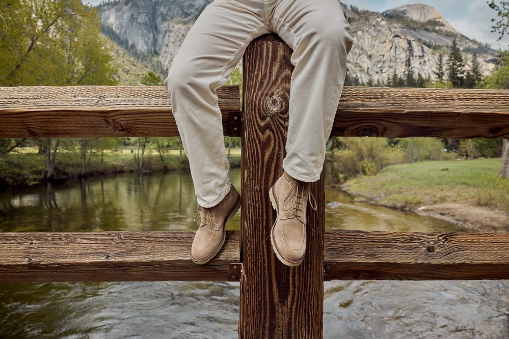 A person is sitting on a wooden railing, wearing light-colored pants and tan suede boots.