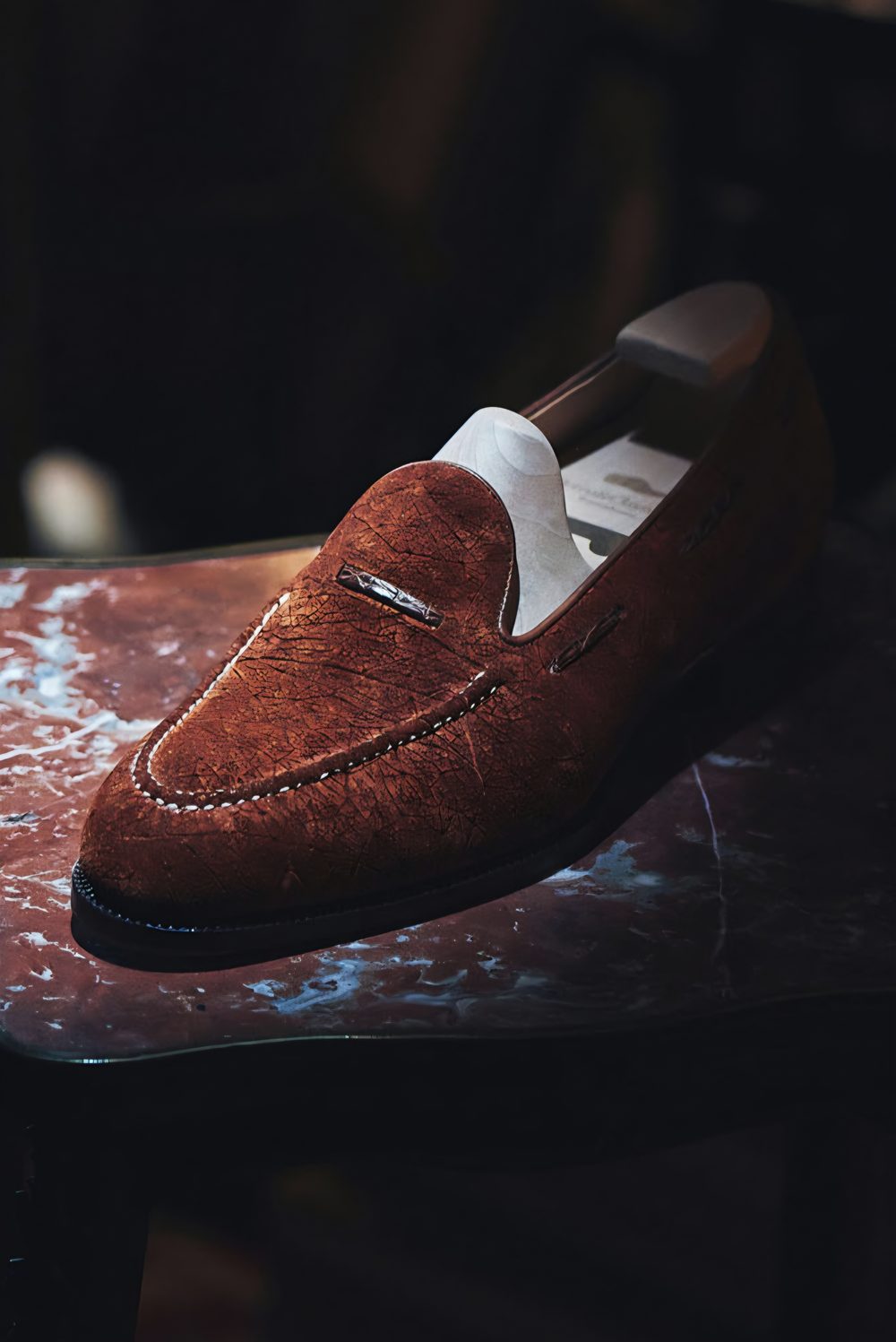 A handmade brown suede loafer shoe with decorative stitching.