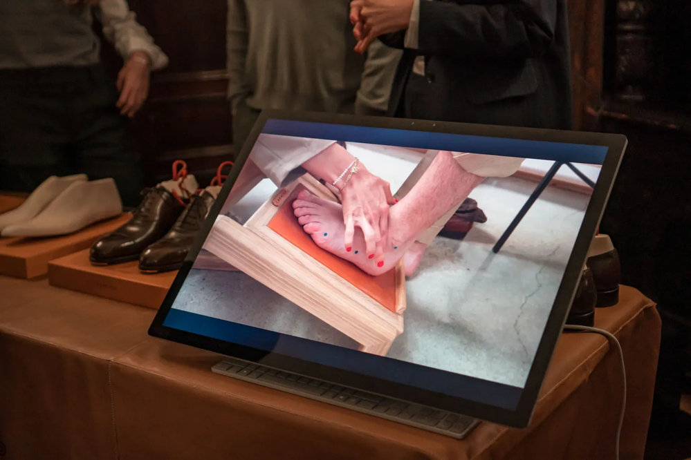 A digital display shows a hand measuring a foot for custom shoe fitting at the Carmina Bespoke Trunk Show.