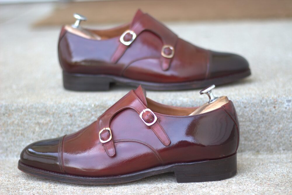 A pair of polished brown leather shoes with silver buckles and shoe trees.