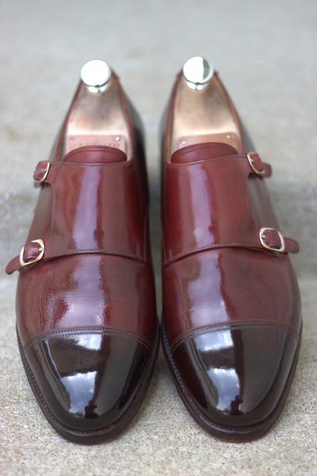 A pair of polished burgundy leather shoes with double buckles and a glossy black toe cap.