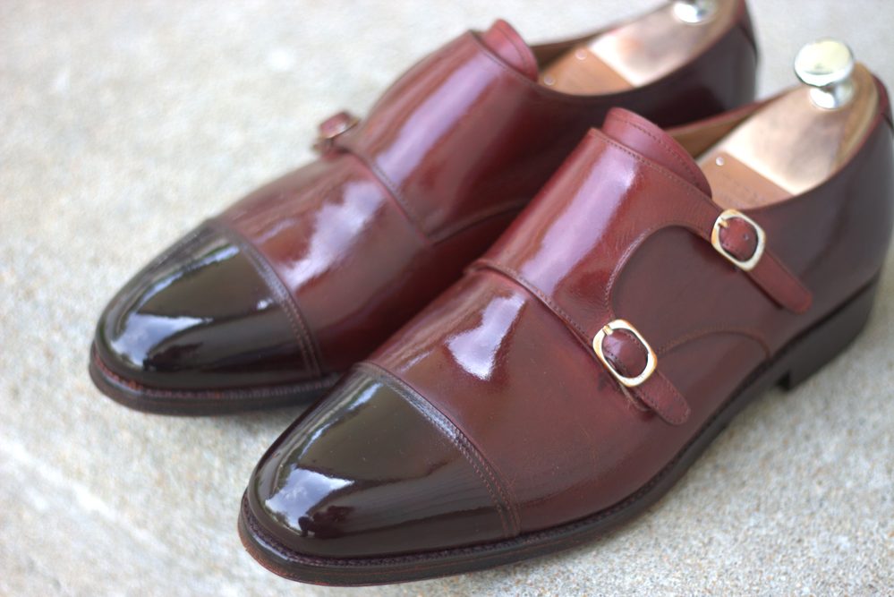 A pair of polished burgundy leather shoes with black patent leather toes and gold buckles.