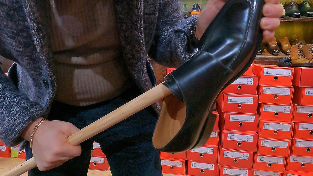 A person is using a wooden stick to stretch a black leather shoe.