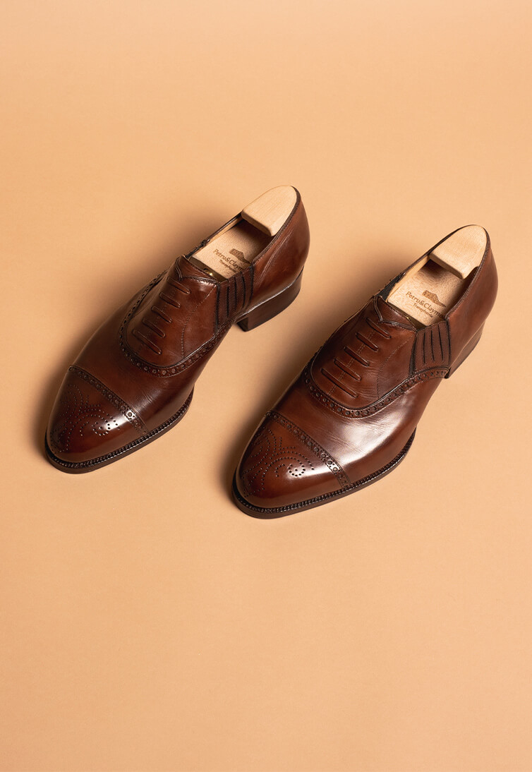 A pair of brown handmade leather shoes with decorative perforations and a polished finish.