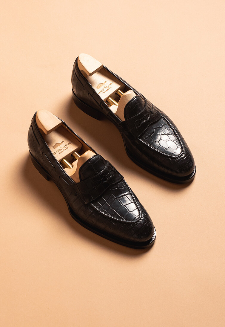 Black leather loafers with a crocodile texture and wooden shoe trees inside.